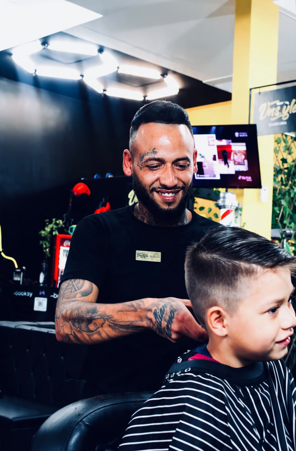 Barbeiro sorrindo durante um corte de cabelo infantil na VNS Style